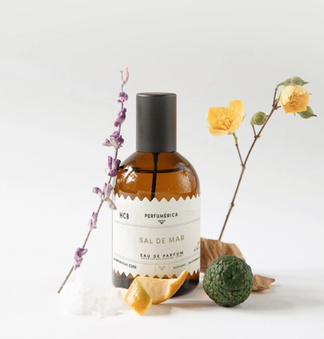 Sal De Mar Eau de Parfum displayed with botanical elements including dried sage, citrus, and flowers, highlighting its natural marine-inspired notes.
