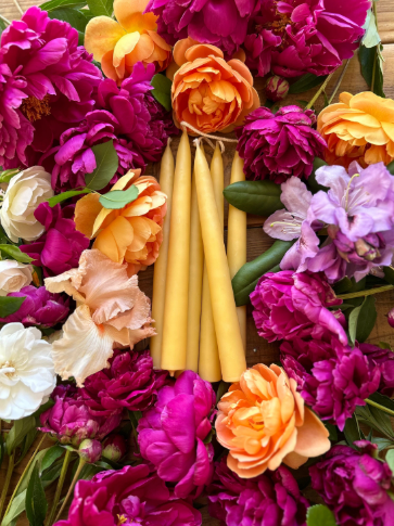 Close-up of the Busy Bees Candle Co. 100% pure beeswax taper candles with cotton wicks, highlighting the smooth hand-dipped texture surrounded by flowers.