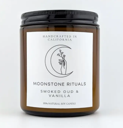 A Moonstone Rituals soy wax candle in a sleek glass jar with a minimalist label and a natural wooden wick in Smoked Oud & Vanilla scent.