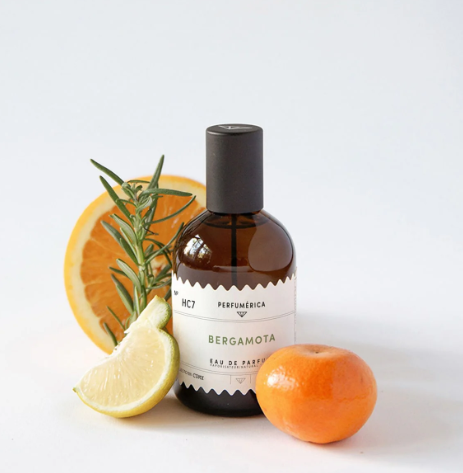 The Bergamota Eau de Parfum bottle surrounded by fresh citrus slices and sprigs of rosemary, highlighting its bright, natural ingredients.
