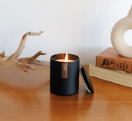 A beautifully lit Mahogany + Cashmere soy candle, showcasing its warm glow and elegant matte black tumbler.