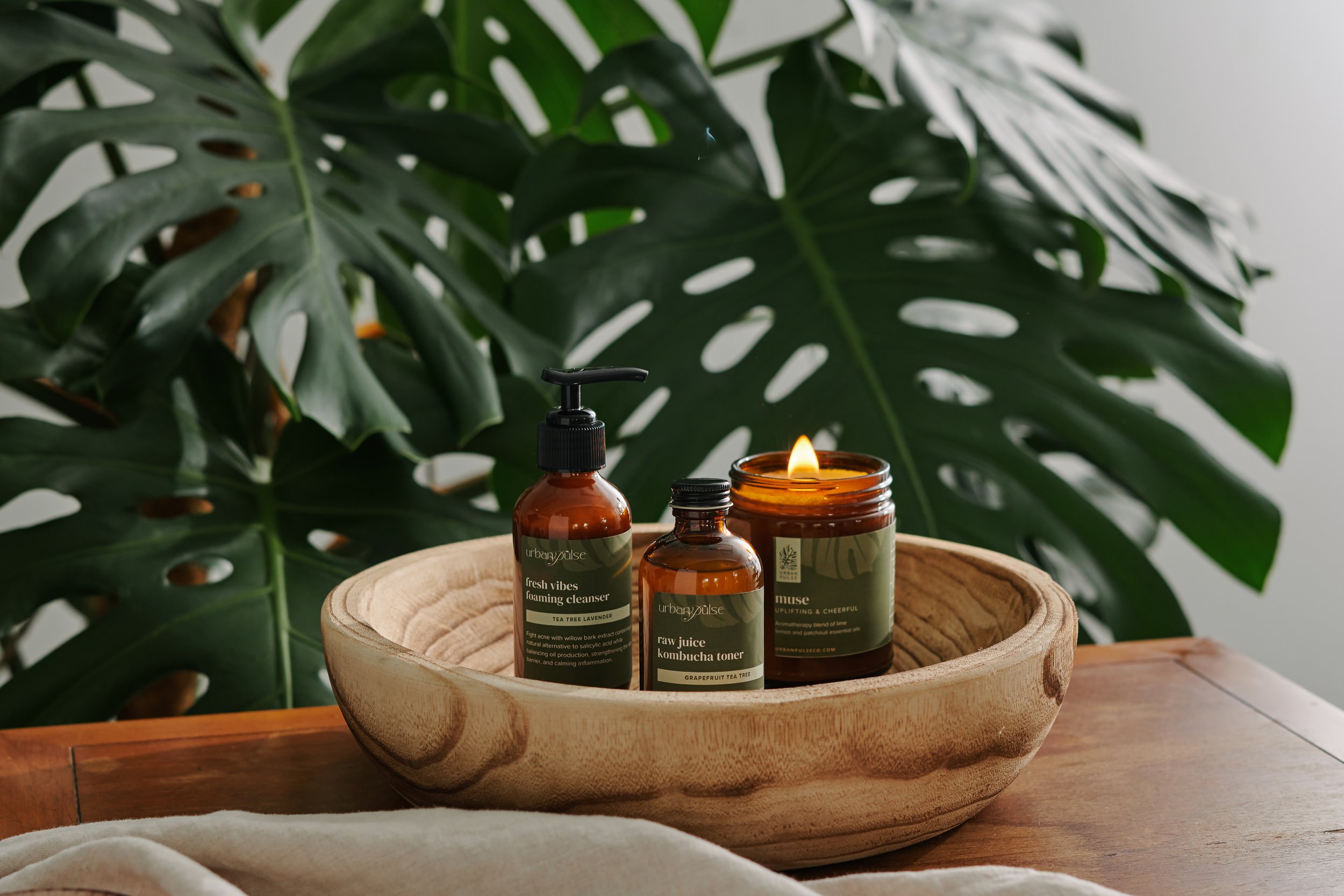 Urban Pulse bath and body products photographed by Philadelphia photographer Tina Crespo, featuring products inside handmade wooden bowl with a plant background.