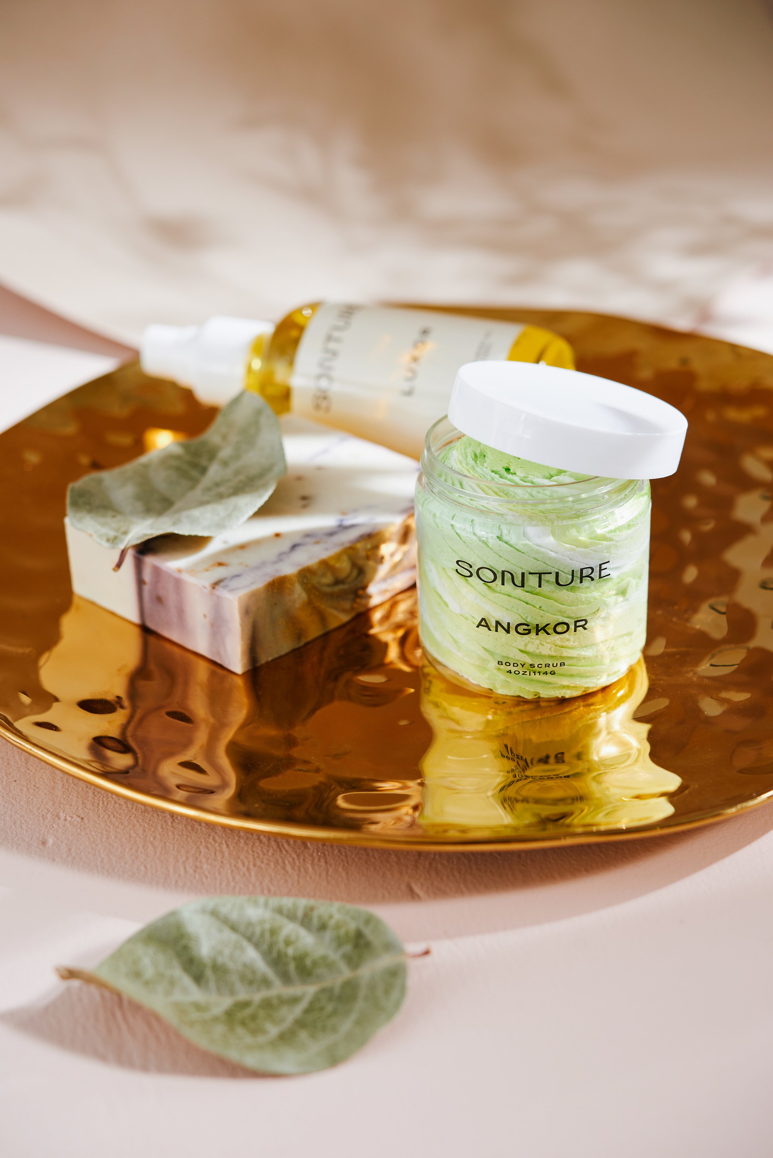 Sonture Beauty bath and body products photographed by Philadelphia photographer Tina Crespo, showcasing body scrub and soap on gold plate.