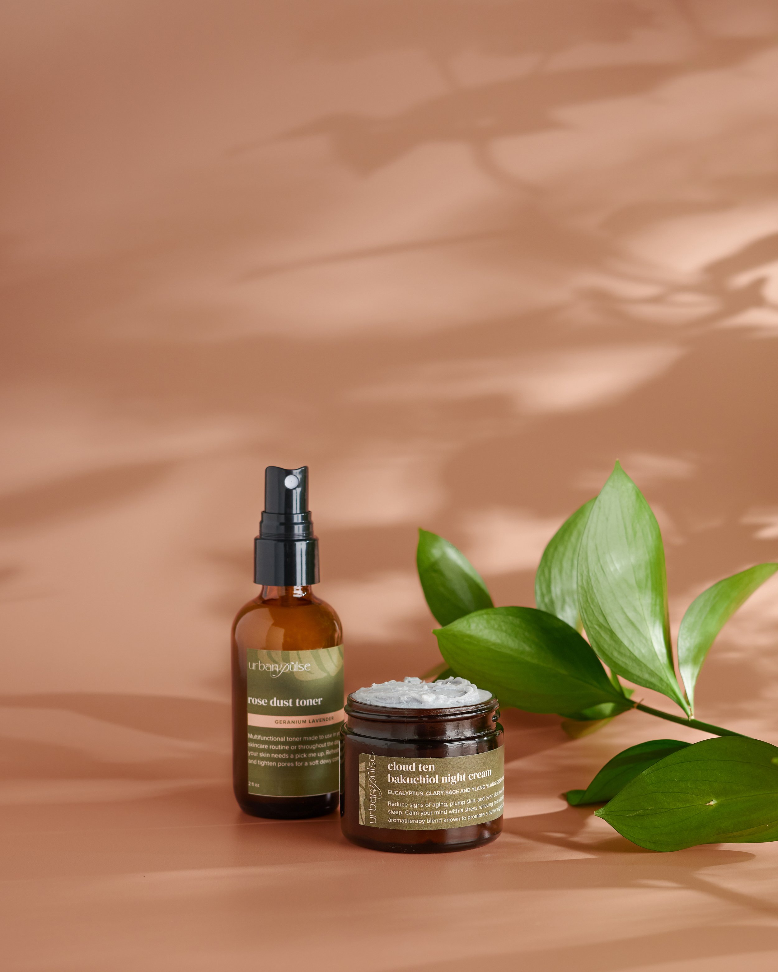Urban Pulse bath and body products photographed by Philadelphia photographer Tina Crespo, showcasing body cream and body oil on a tan background with greenery.