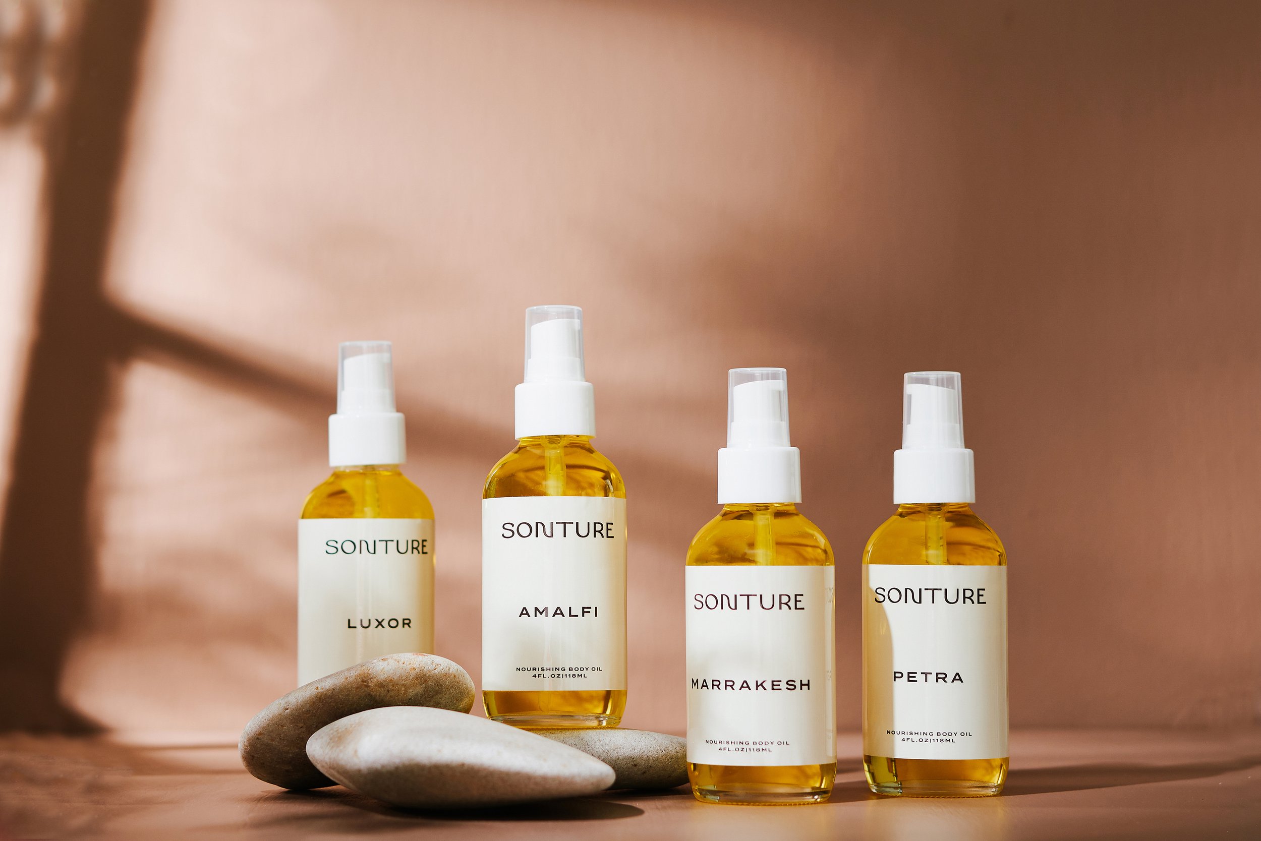 A group of golden body oils photographed against a warm brown background with deep shadows. Photographed by Tina Crespo