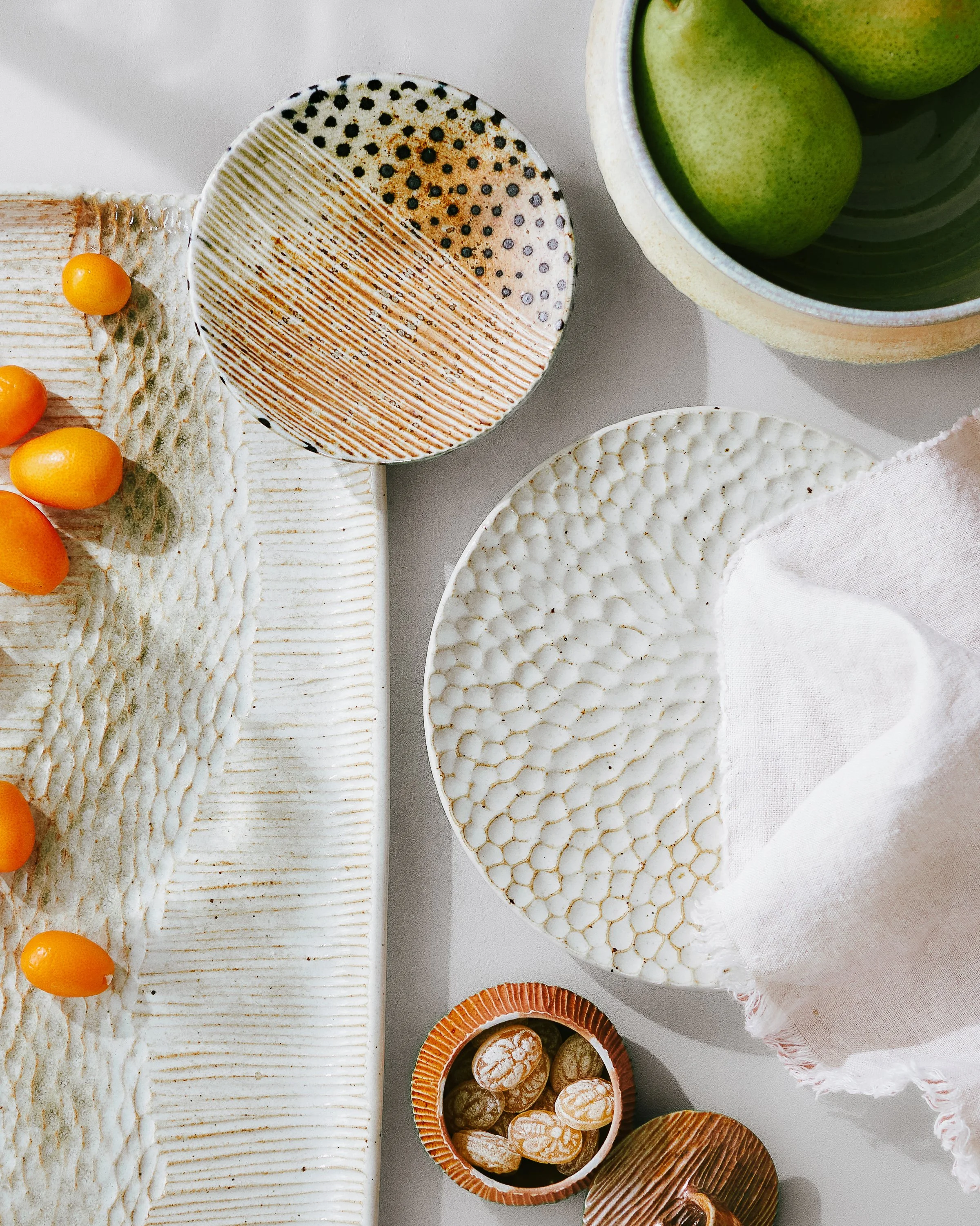 Handmade textured plates and bowls with pears, kumquats and a linen napkin