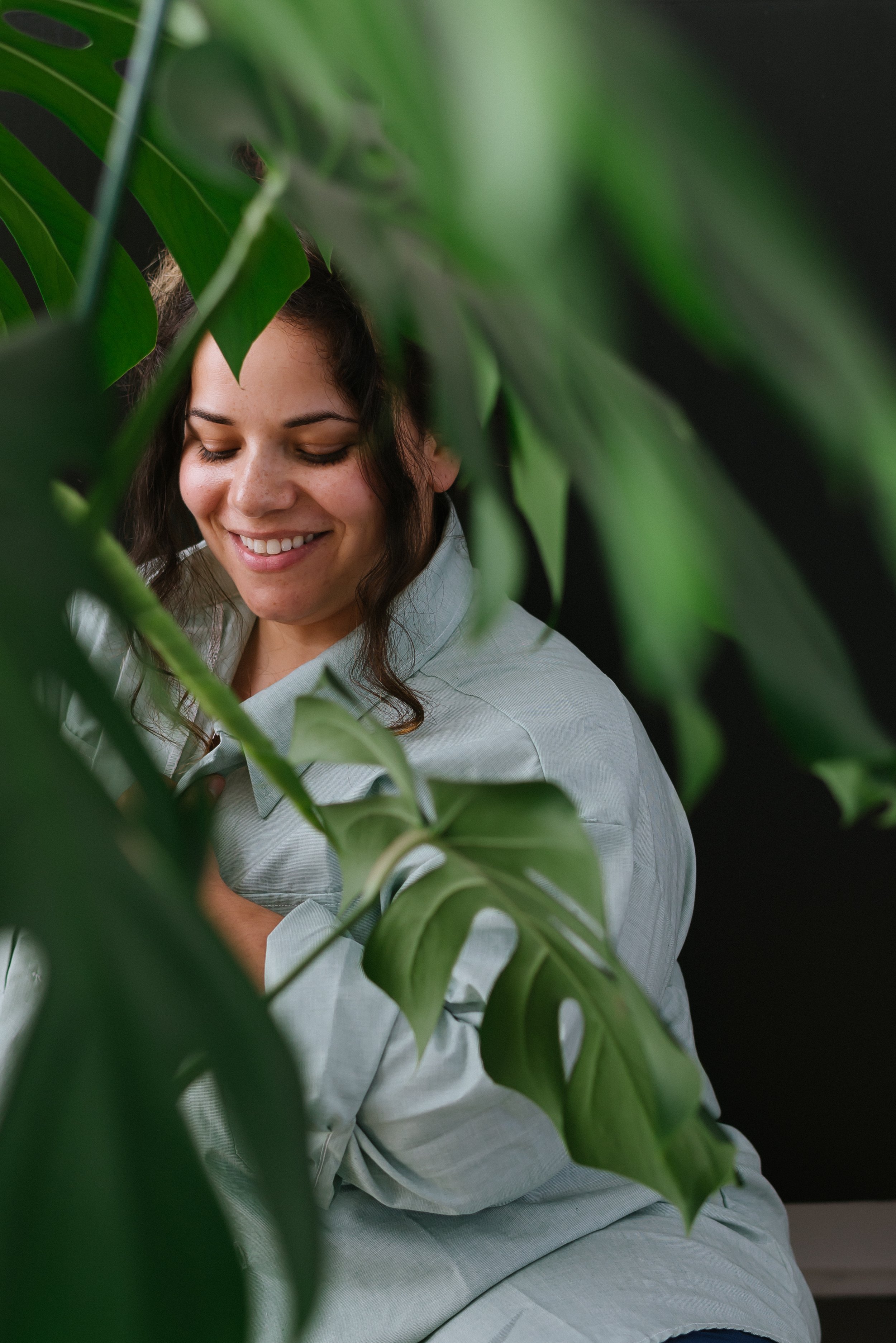 A portrait of Tina Crespo, a Puerto Rican Philadelphia Commercial Photographer behind Monstera leaves