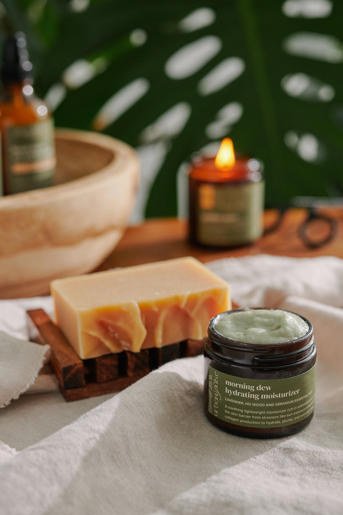 Urban Pulse bath and body products photographed by Philadelphia photographer Tina Crespo, showcasing body cream and soap on a linen with monstera in the background.