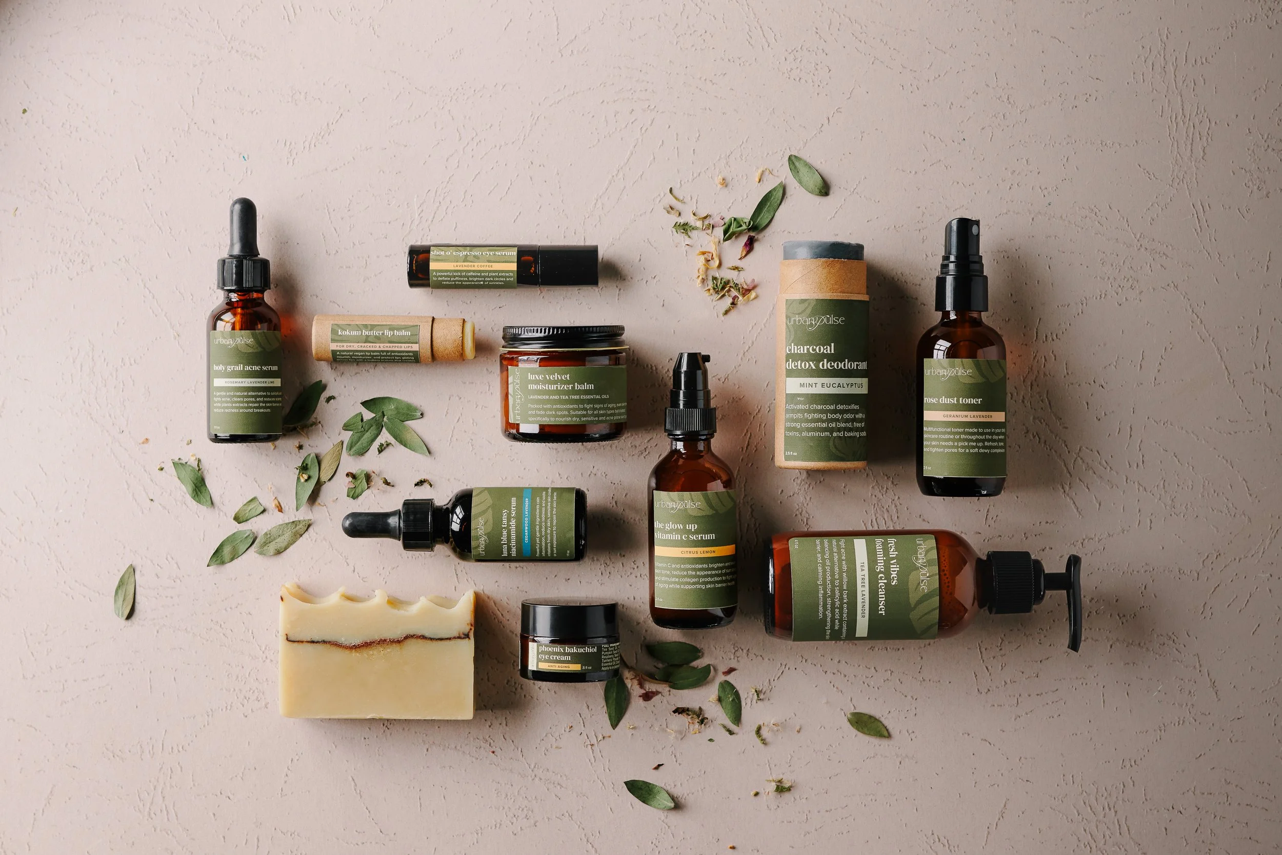 A flatlay of skincare products on a textured cream colored background with loose tea leaves and petals. Photographed by Tina Crespo.