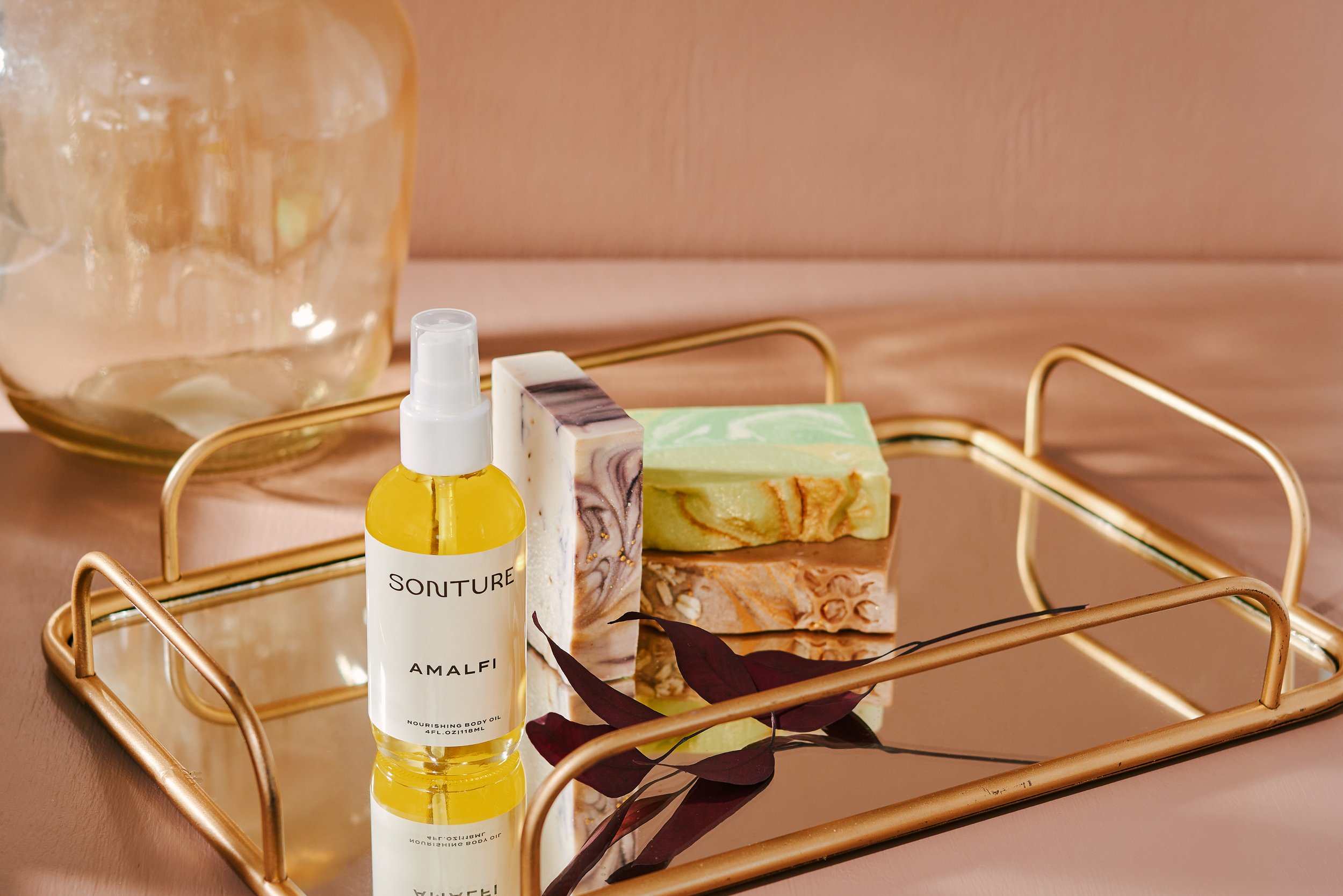 Sonture Beauty bath and body products photographed by Philadelphia photographer Tina Crespo, showcasing body oil and soaps on mirror tray.