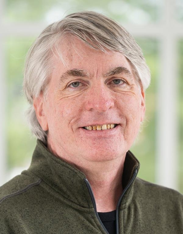 Portrait of a man with gray hair wearing a dark green shirt.
