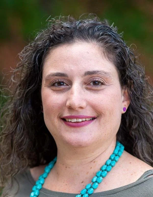 Portrait of a woman with wavy dark hair wearing a turquoise necklace.