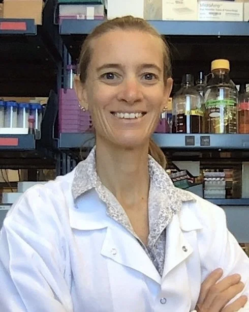 Portrait of a woman with blonde hair wearing a white lab coat.
