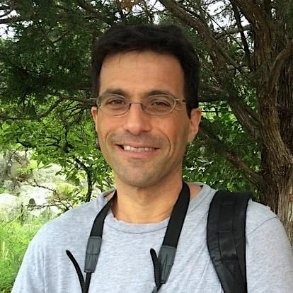 Portrait of a man with dark hair wearing glasses and a gray t-shirt.