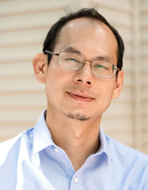 Portrait of a man with black hair who is wearing a light blue shirt and glasses.