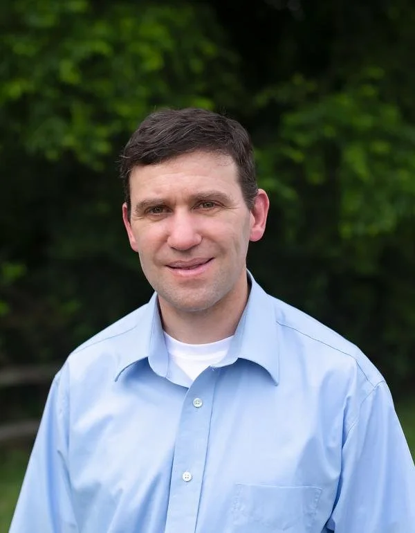 Portrait of a man with brown hair wearing a light blue shirt.