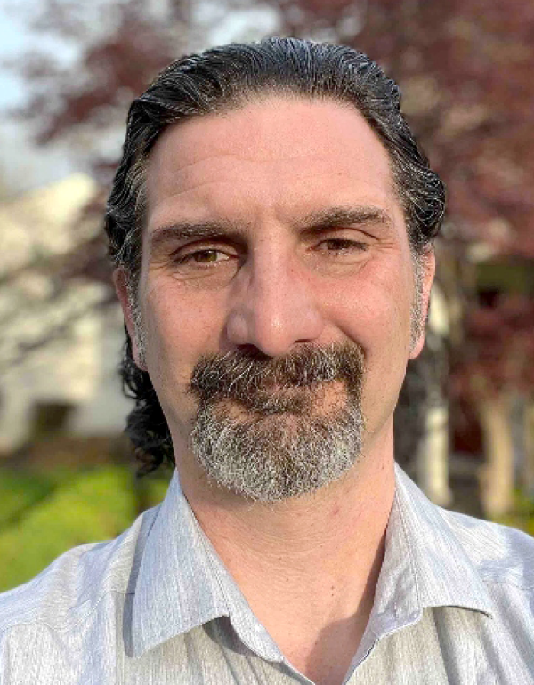 Portrait of a man with brown / gray hair wearing a light gray shirt.