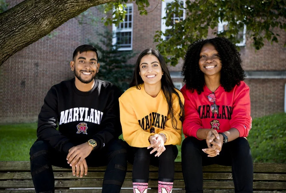 Three UMD students in corresponding sweaters colored in black, yellow, and red.