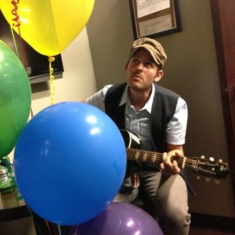 Gregory Alan Isakov playing guitar backstage surrounded by colorful balloons.