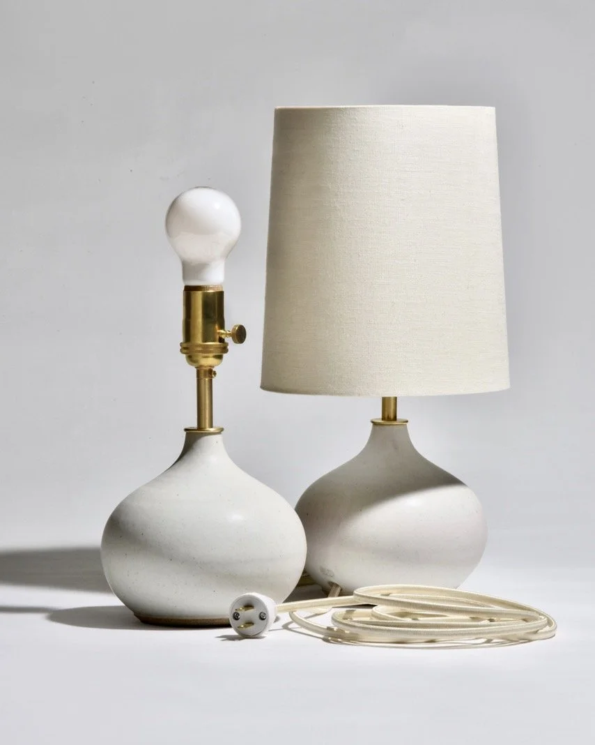 A pair of lamps in Eggshell with unfinished cast brass hardware, linen rolled edge shades and cloth-covered power cord. Just 16&quot; tall, these lamps work well on a desk or bedside table. The hardware will gain patina over time, adding character to