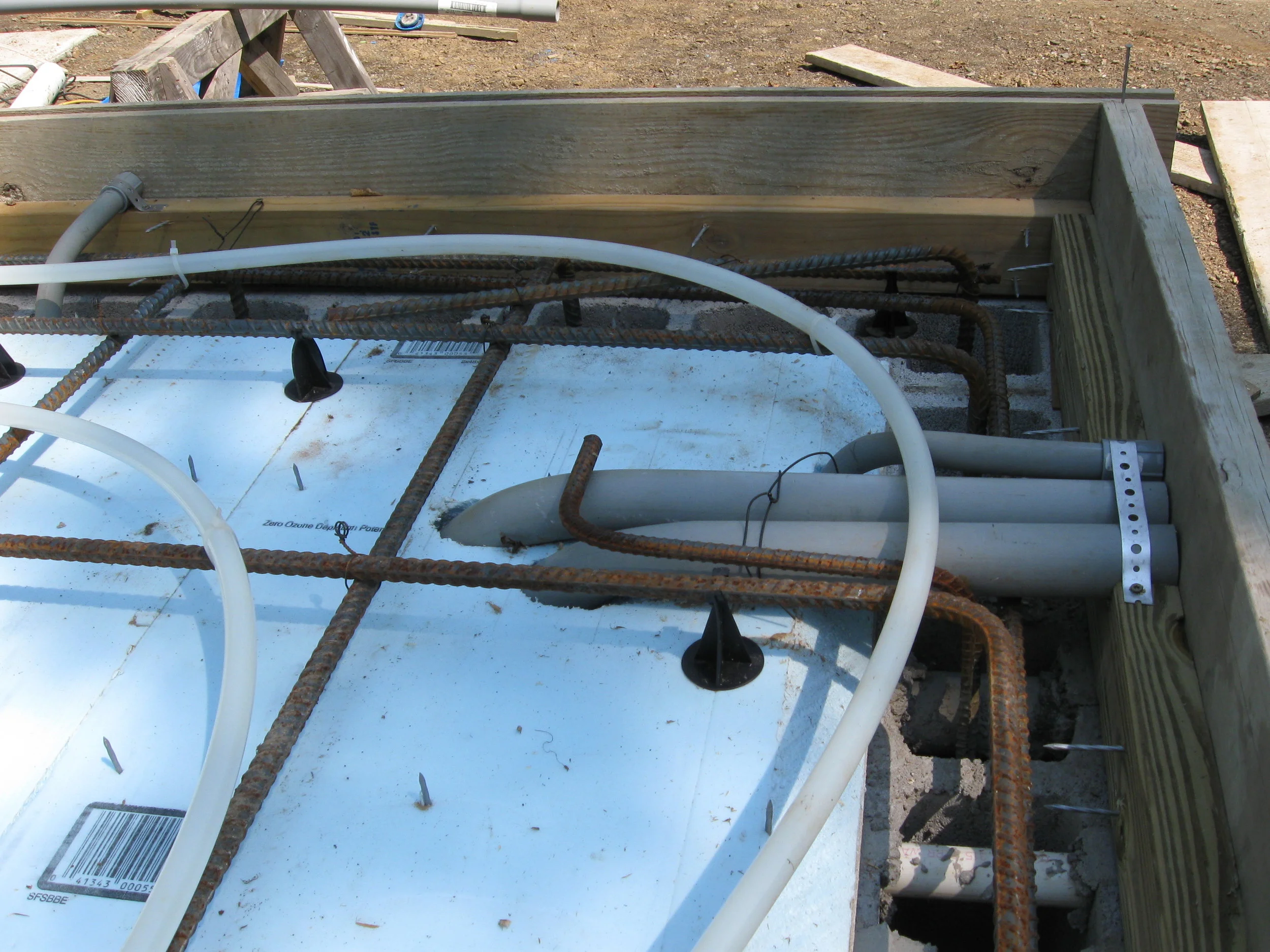  Detail of the preparations for pouring the floor, showing chases for utility service, a perimeter board for attaching the SIPs, and pex tubing for radiant floor heating. 