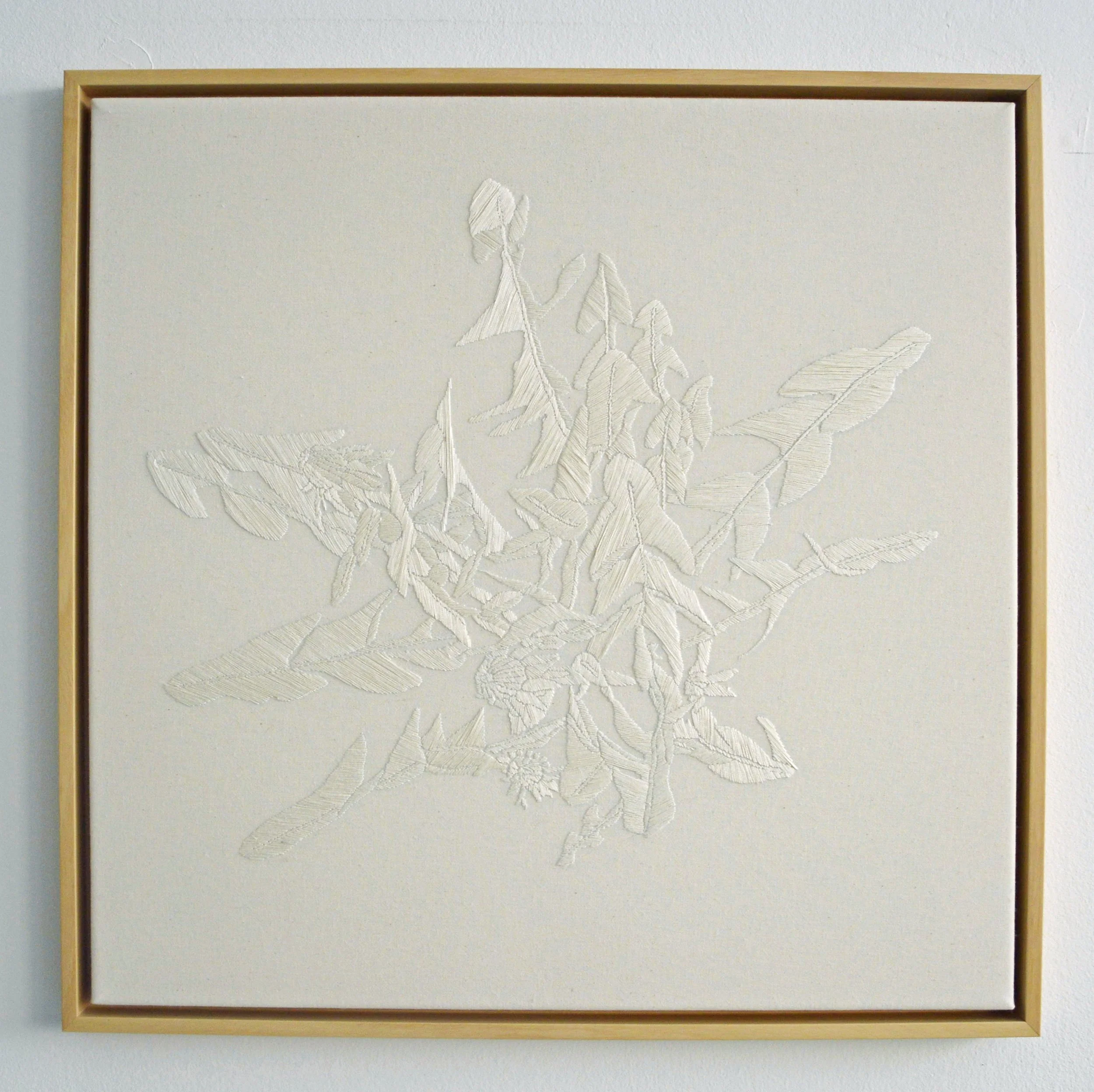 Ein weißes, gerahmtes Rahmentshirt mit geprägtem Blumen- und Blattmuster an einer weißen Wand.