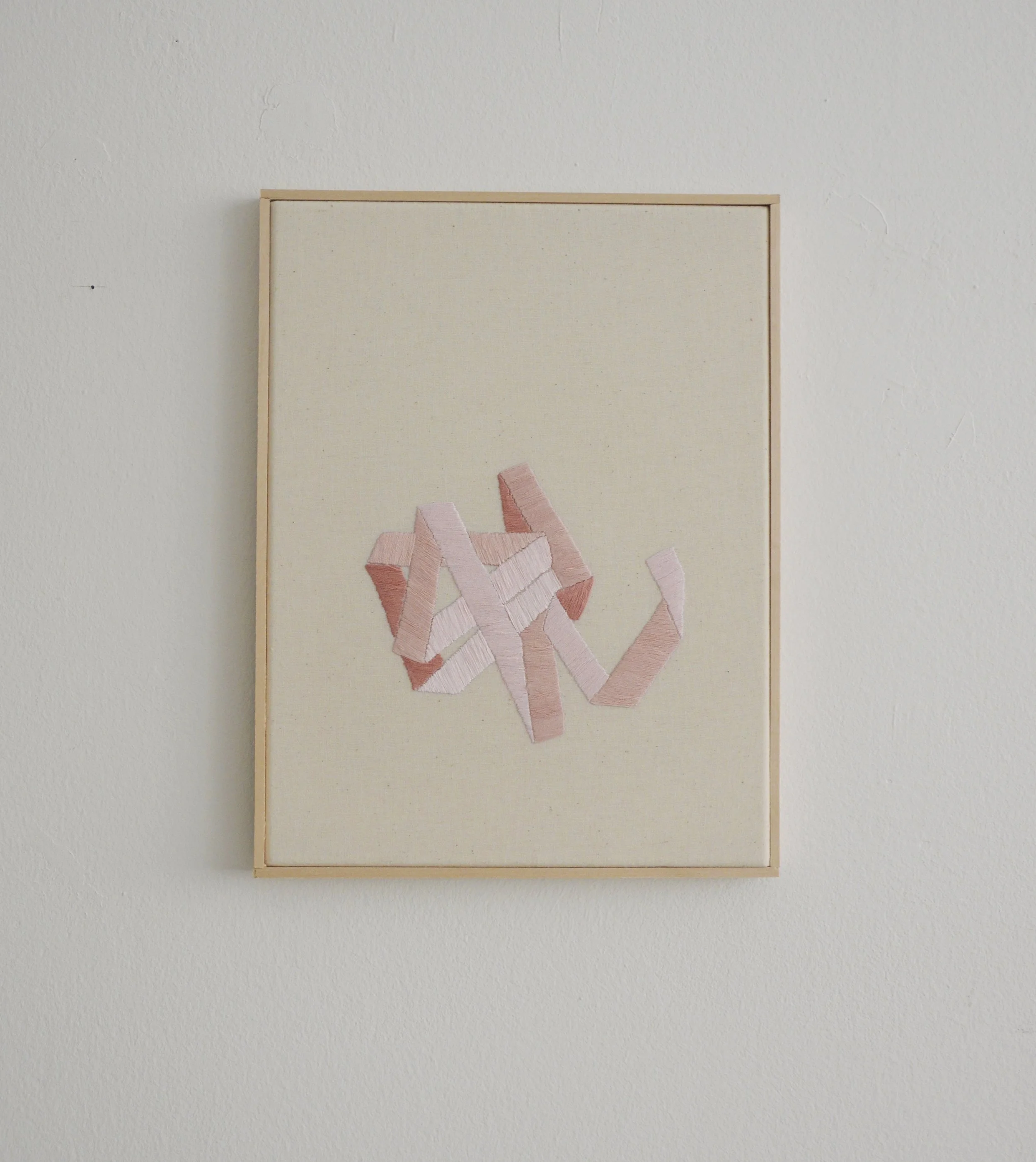 Abstraktes Wandbild mit rosa und weißen Stoffstreifen auf einem weißen Hintergrund.