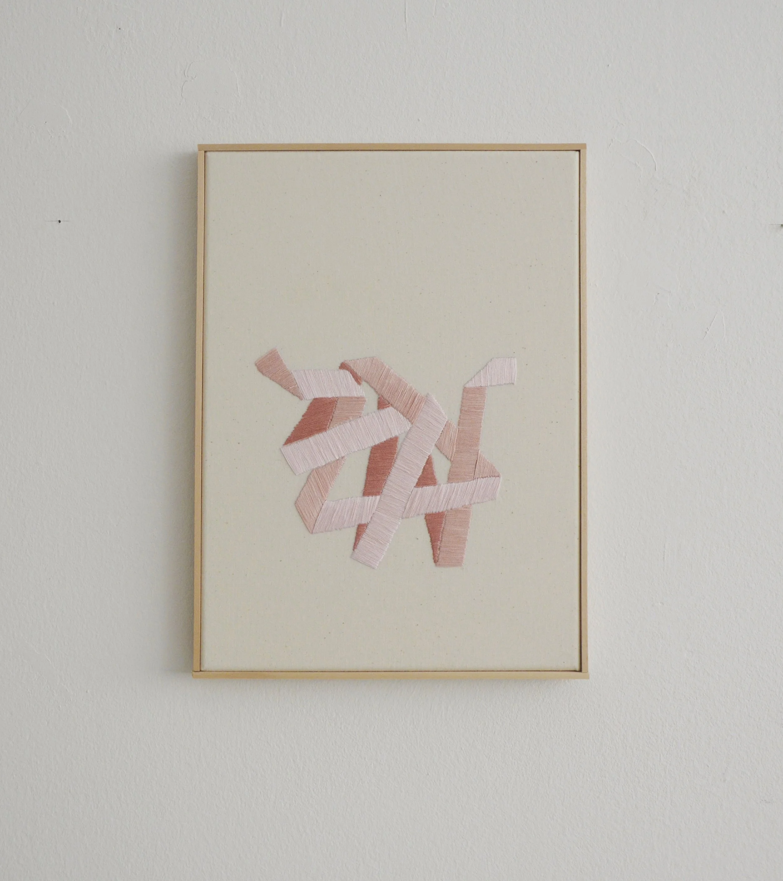 Abstraktes Kunstwerk mit rosa Stoffstreifen auf weißem Hintergrund in einem Rahmen.