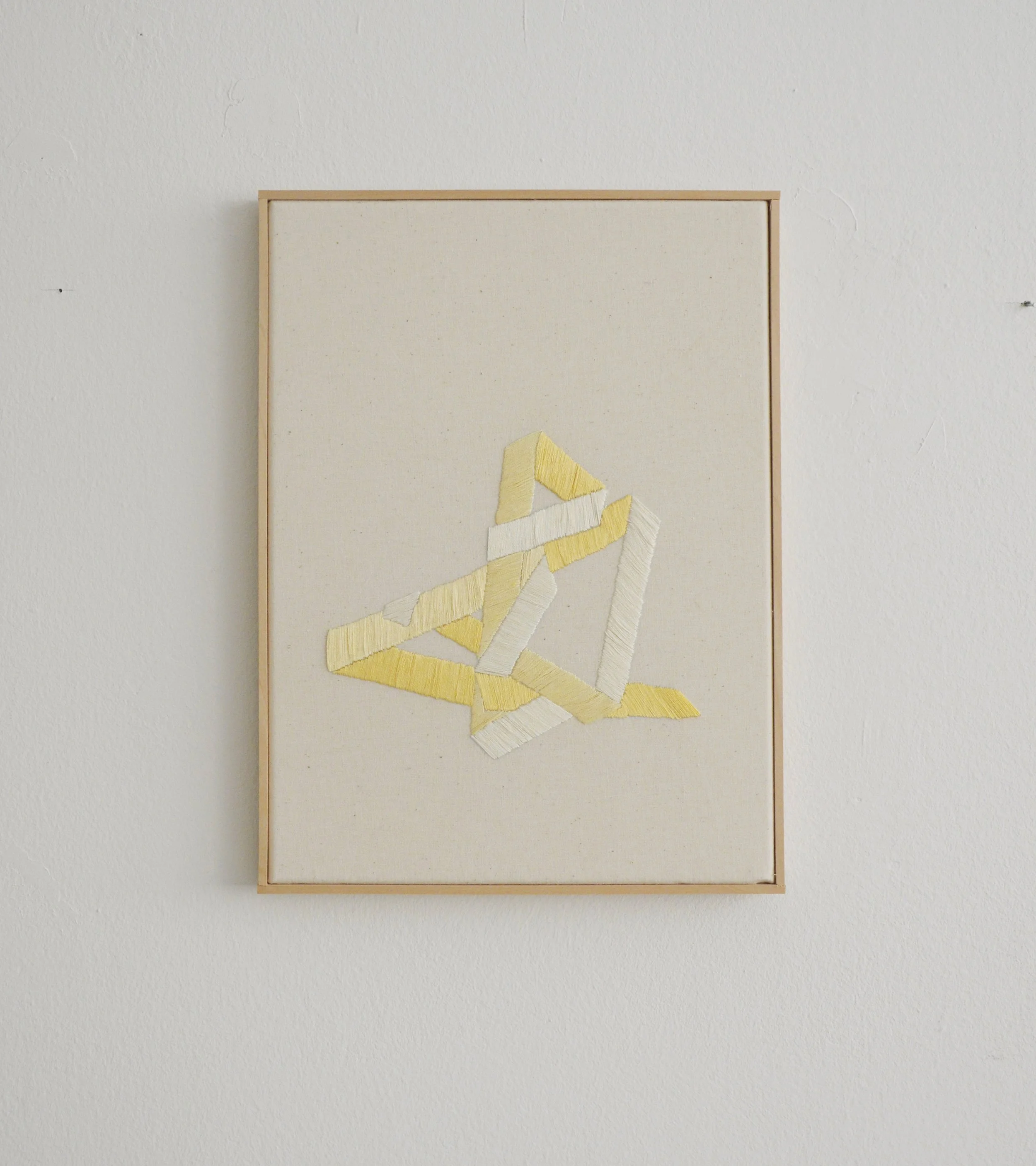 Ein Kunstwerk aus verschiedenen gelben und weißen Stoffstreifen, die zu einer abstrakten Form auf einem weißen Hintergrund zusammengenäht sind.