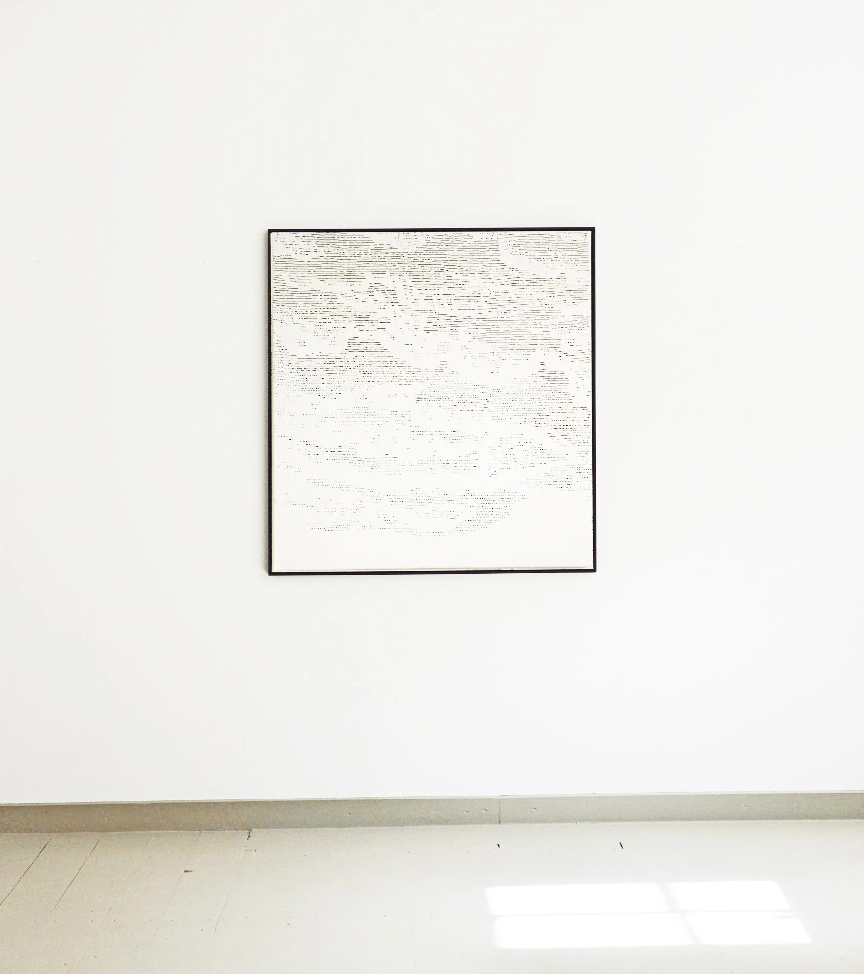 Ein Kunstwerk mit schwarzen Linien auf weißem Hintergrund in einem Bilderrahmen, an einer weißen Wand in einem Ausstellungsraum aufgehängt.