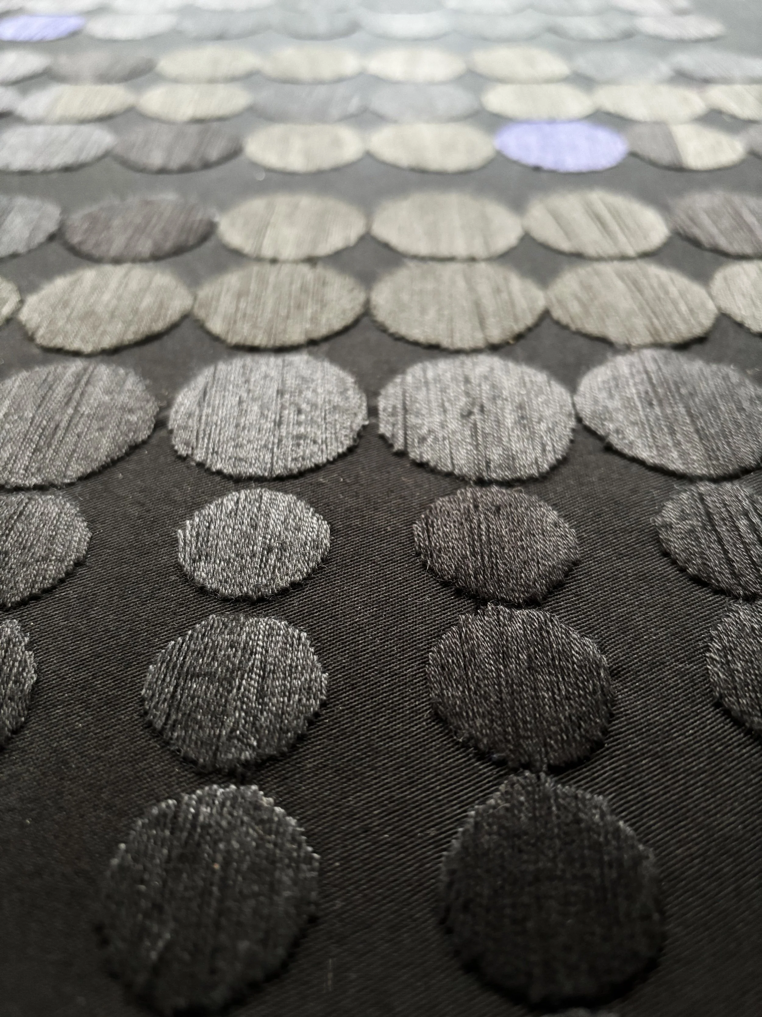 Nahaufnahme eines Stoffes mit metallic-ähnlichen, runden, gewebten Mustern in Silber- und Grautönen.