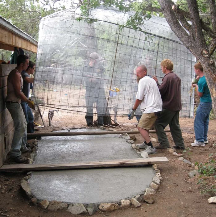 Concrete is poured sloping to a center drainpipe. The spigot pipe, also imbedded in the slab, sticks up six inches to pull water out from above any sludge buildup at the bottom of the tank. The completed skeleton is placed on the slab and plastered before the concrete sets up to prevent leakage where the wall meets the floor.
