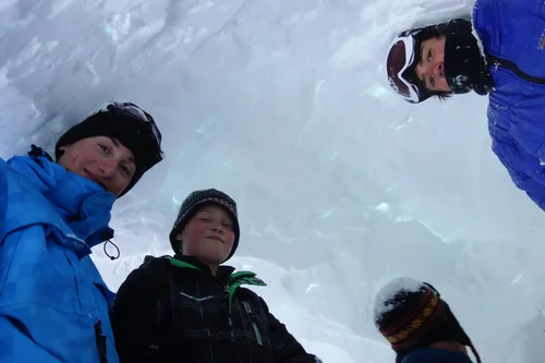 Kyle Totman, Alex Keltner, and Cade Harris stand tall in their newly dug quinzee while instructor Scott Laidlaw inspects
