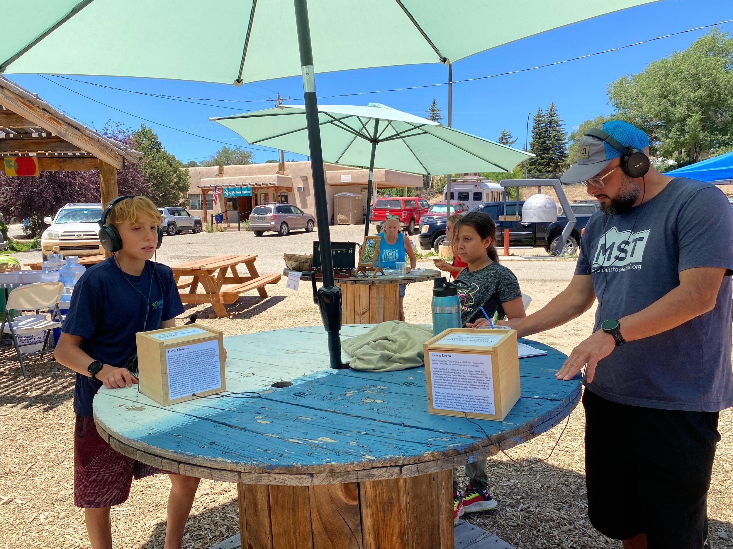 Family listening to the story boxes at the Questa Farmers Market