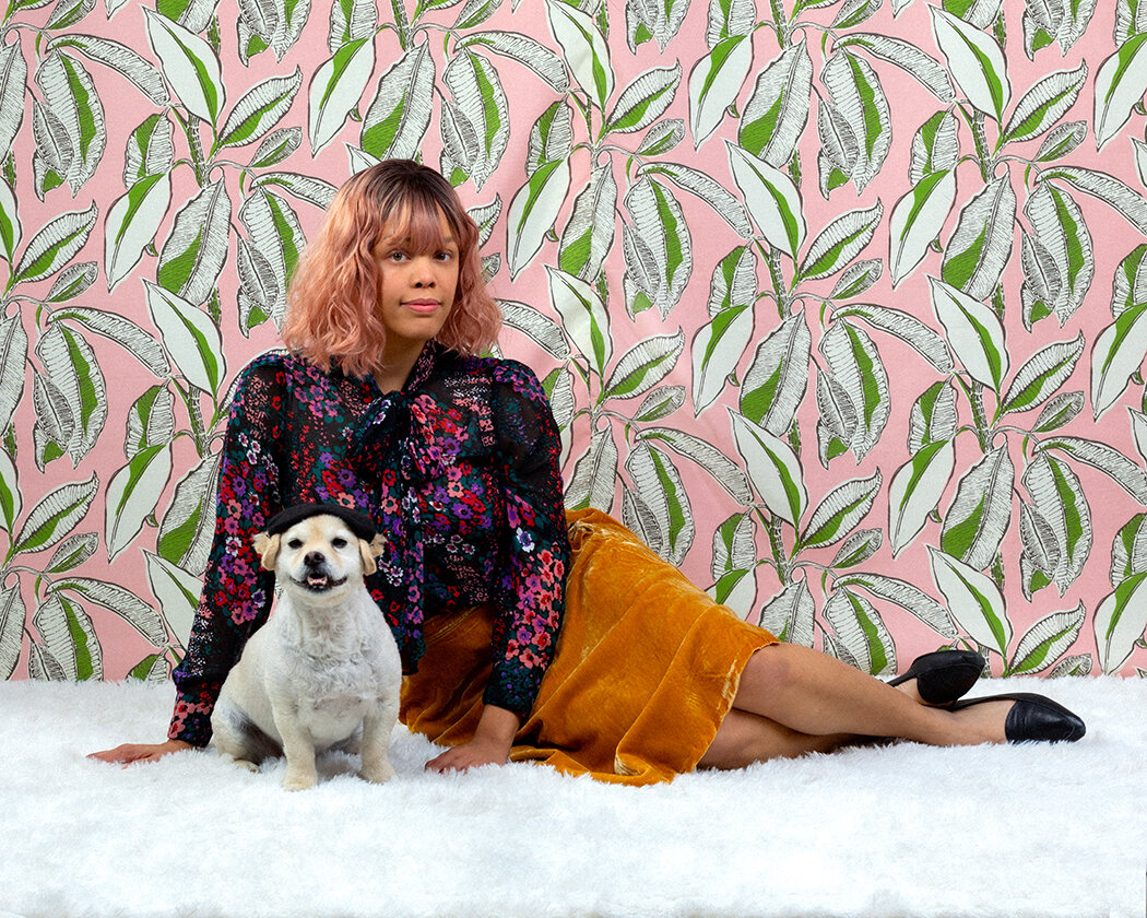 Woman in Modcloth 60s outfit sits with dog on white shag rug and pink palm leaves backdrop by Danielle Spires