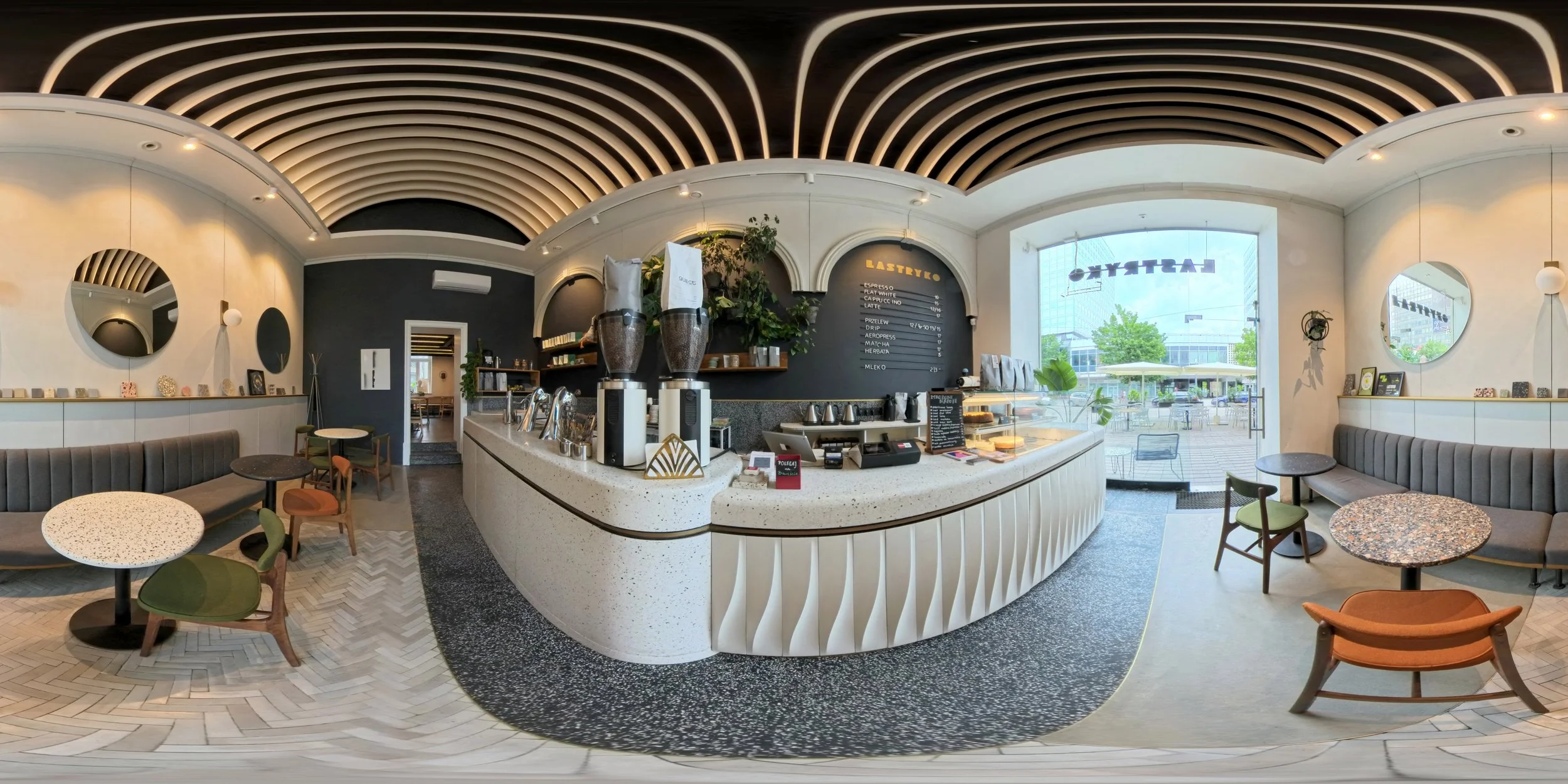 Interior of a modern coffee shop with a curved white counter, coffee brewing equipment, black and white decor, seating area with tables and chairs, large window showing outdoor seating, and minimalistic decorations.
