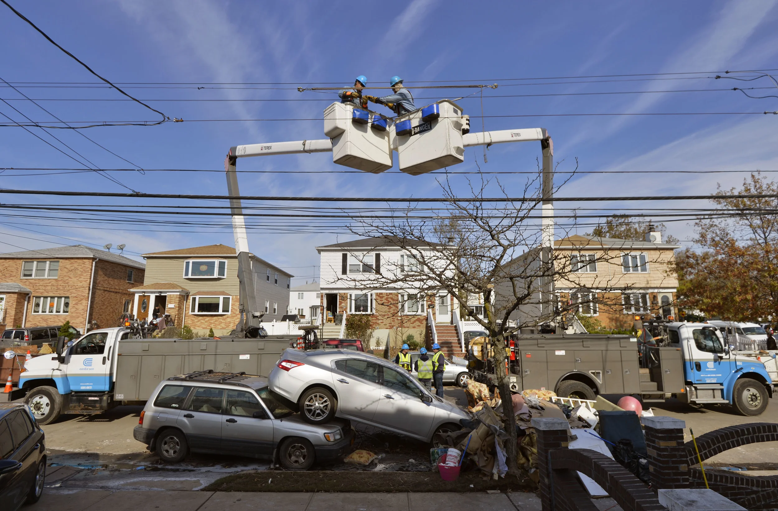 Crews from ConEdison reattach power lines over the two stacked cars as they restore power in store ravanged Staten Island.