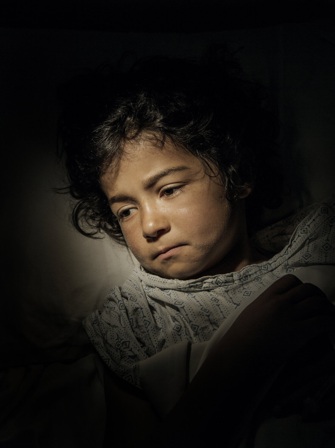  Bibi Najla, age 7, lies in a hospital bed recovering from a bullet wound to her belly. She was shot during fighting between Taliban and government forces in Logar Province, Afghanistan, 2016. 