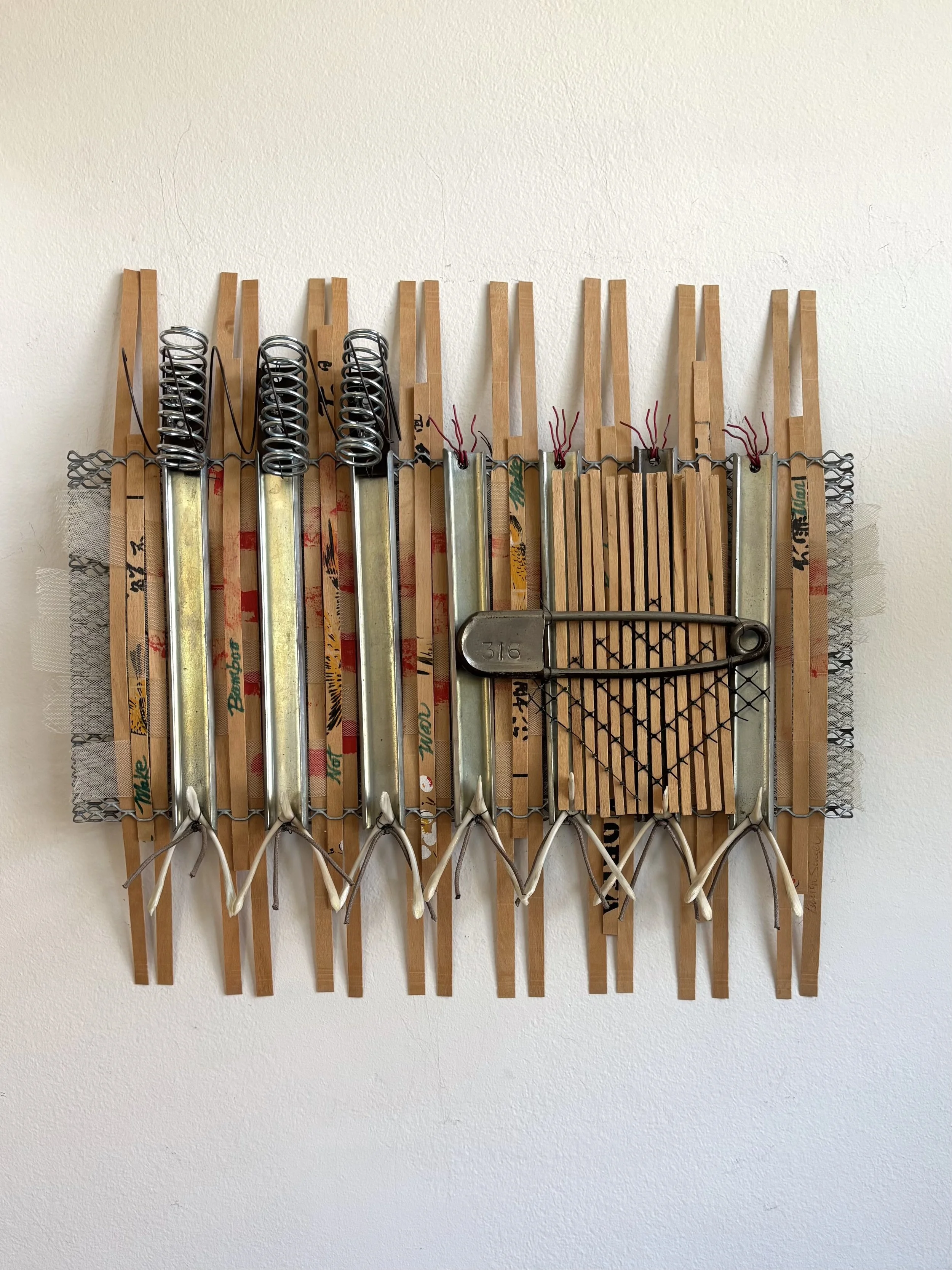  Mixed Media Construction:  Deconstructed antique Korean bamboo fan, bamboo strips, mesh, found objects, chicken bones, industrial safety pin, ribbon, wire 12’ x 13’ x 2”.  This piece addresses the dual nature of the North Korean culture and expresse