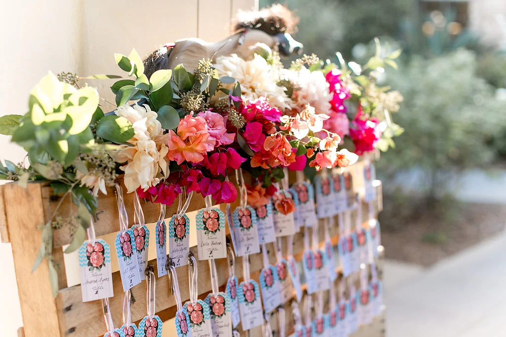 Bohemian wedding escort card display with floral garland by Compass Floral | Estancia Hotel & Spa, La Jolla.