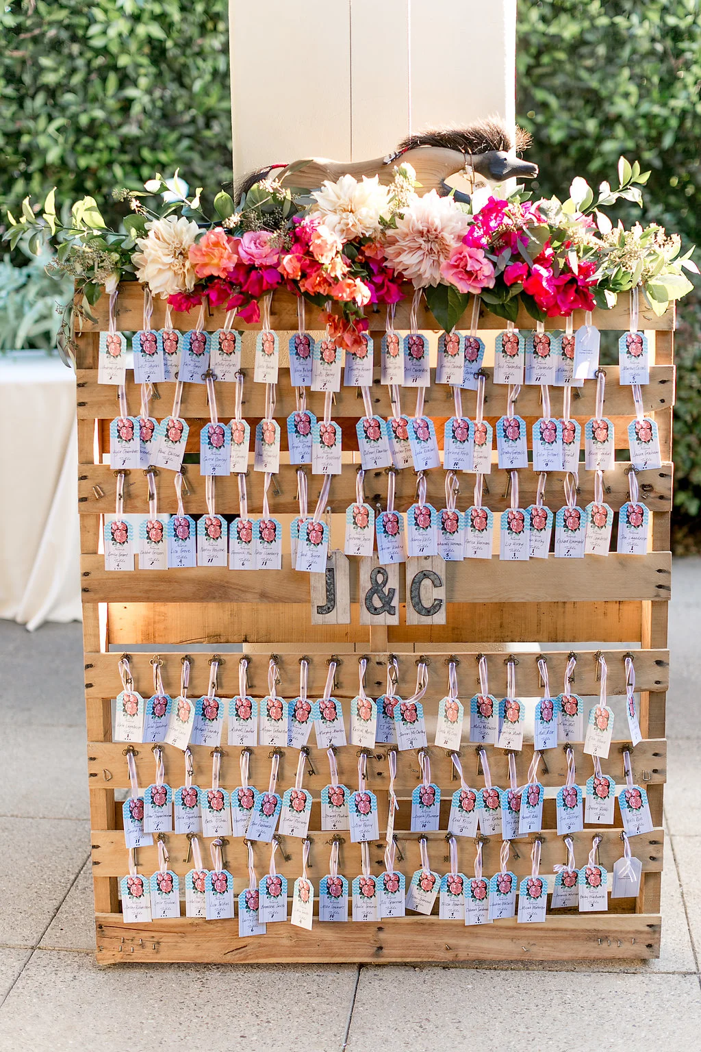 Bohemian wedding escort card display with floral garland by Compass Floral | Estancia Hotel & Spa, La Jolla.