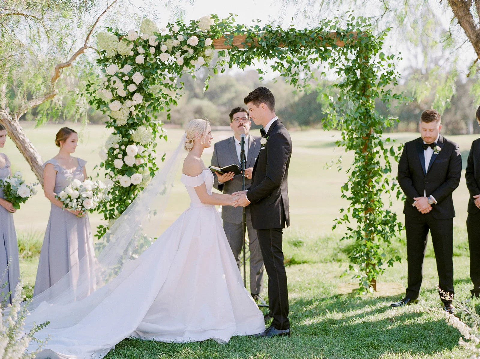 Bride and groom under greenery & white flower covered arch | Rancho Santa Fe Golf Club | Compass Floral | Wedding Florist in San Diego and Southern California | Rachael McCall Photography