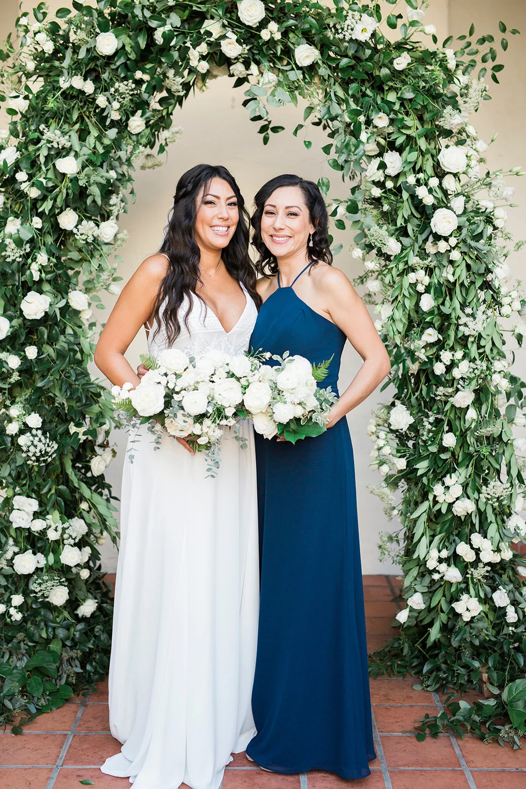 Bride and bridesmaid with white bouquets under greenery arch | Darlington House, La Jolla | Compass Floral | Wedding Florist in San Diego and Southern California | My Sun and Stars Co. Photography