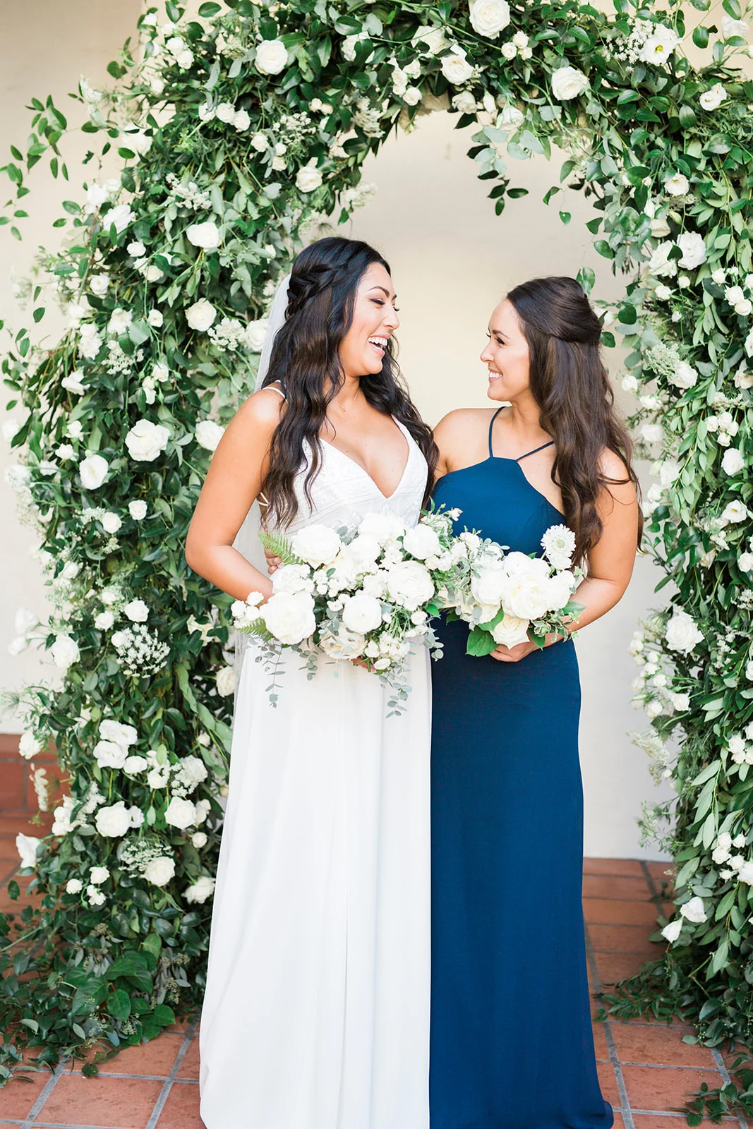 Bride and bridesmaid with white bouquets under greenery arch | Darlington House, La Jolla | Compass Floral | Wedding Florist in San Diego and Southern California | My Sun and Stars Co. Photography