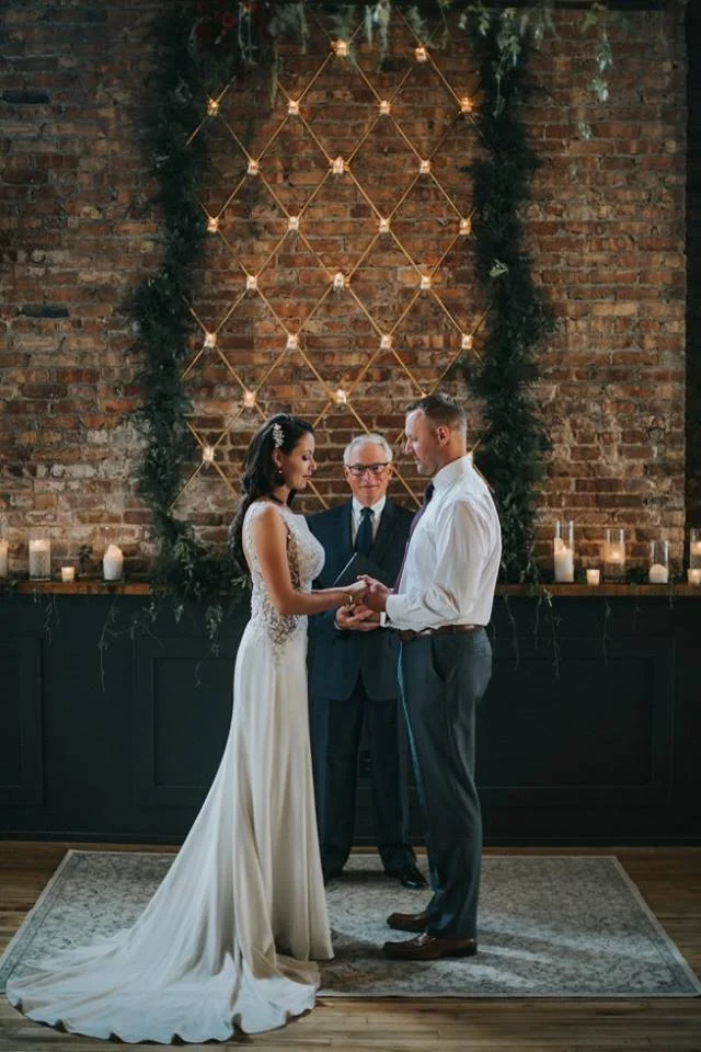 Couple getting married at Mercantile Hall. Bride is wearing a Maggie Sottero gown from Bon Bon Belle. Photo Credits: Floral: Jane Kelly Floral, Photography: Uttke Photography & Design, Hair & Makeup: Raw Salon & Spa Bridal Accessories: Jaxie Bridal, Bridal floral earrings: Jane Kelly Floral