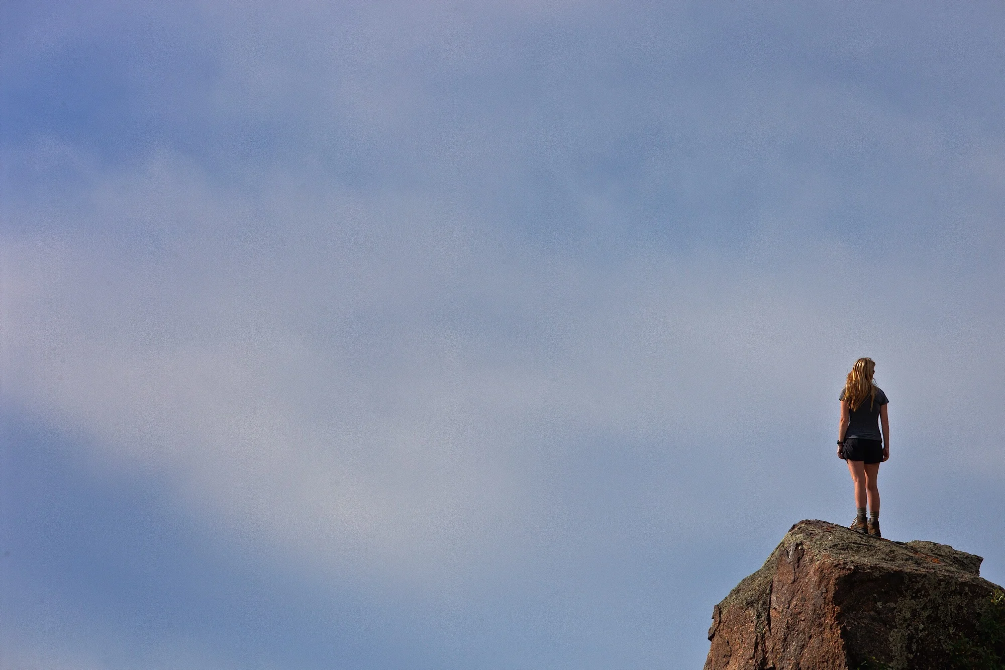 blonde woman atop a large granite rock taking a break from hiking enjoys the scenery.