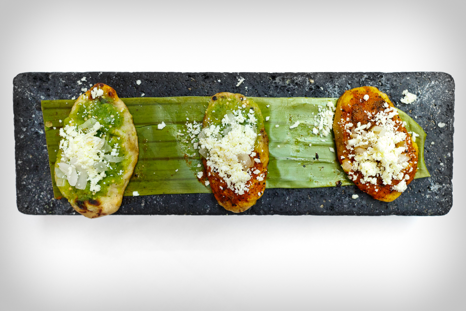 Los tlacoyos con frijol de Chignahuapan - gorditas de maíz rellenas de frijol, con salsa, cebolla, y queso fresco (Griddled black bean corn puffs topped with salsa