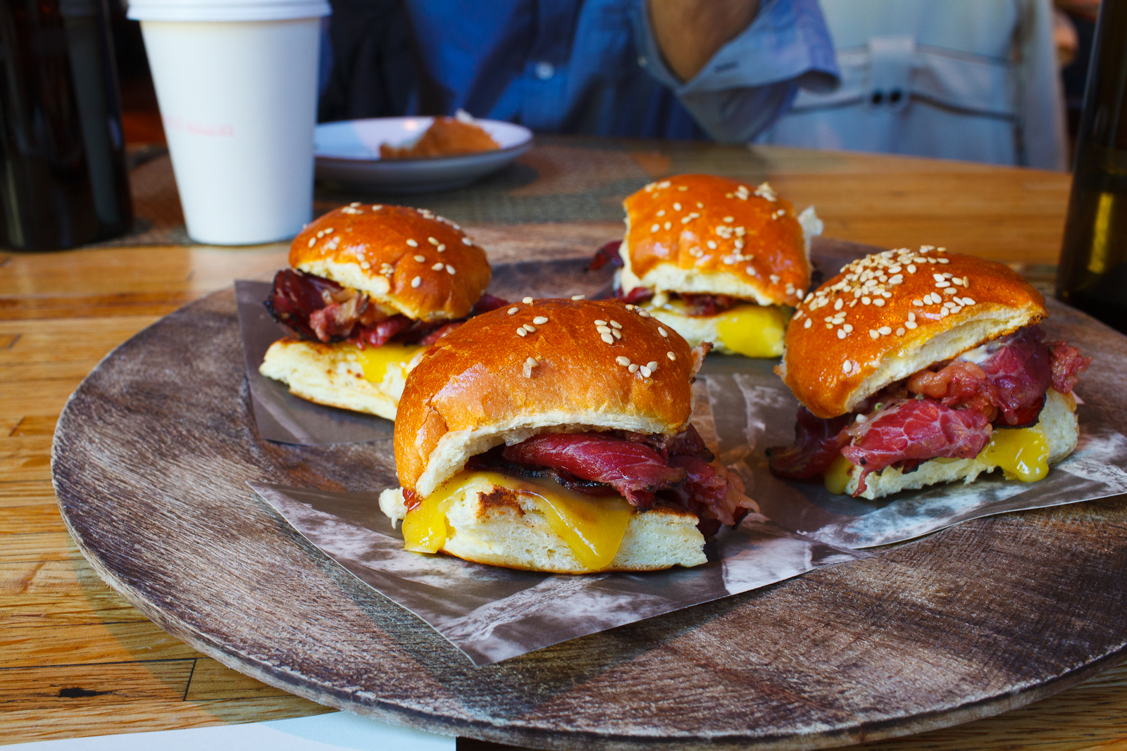 Slices of 45-day dry aged 3-day cured beef with a garlic and black pepper crust smoked for 16-hours on a benne buttermilk bun, cheese, tomato aïoli, garlic