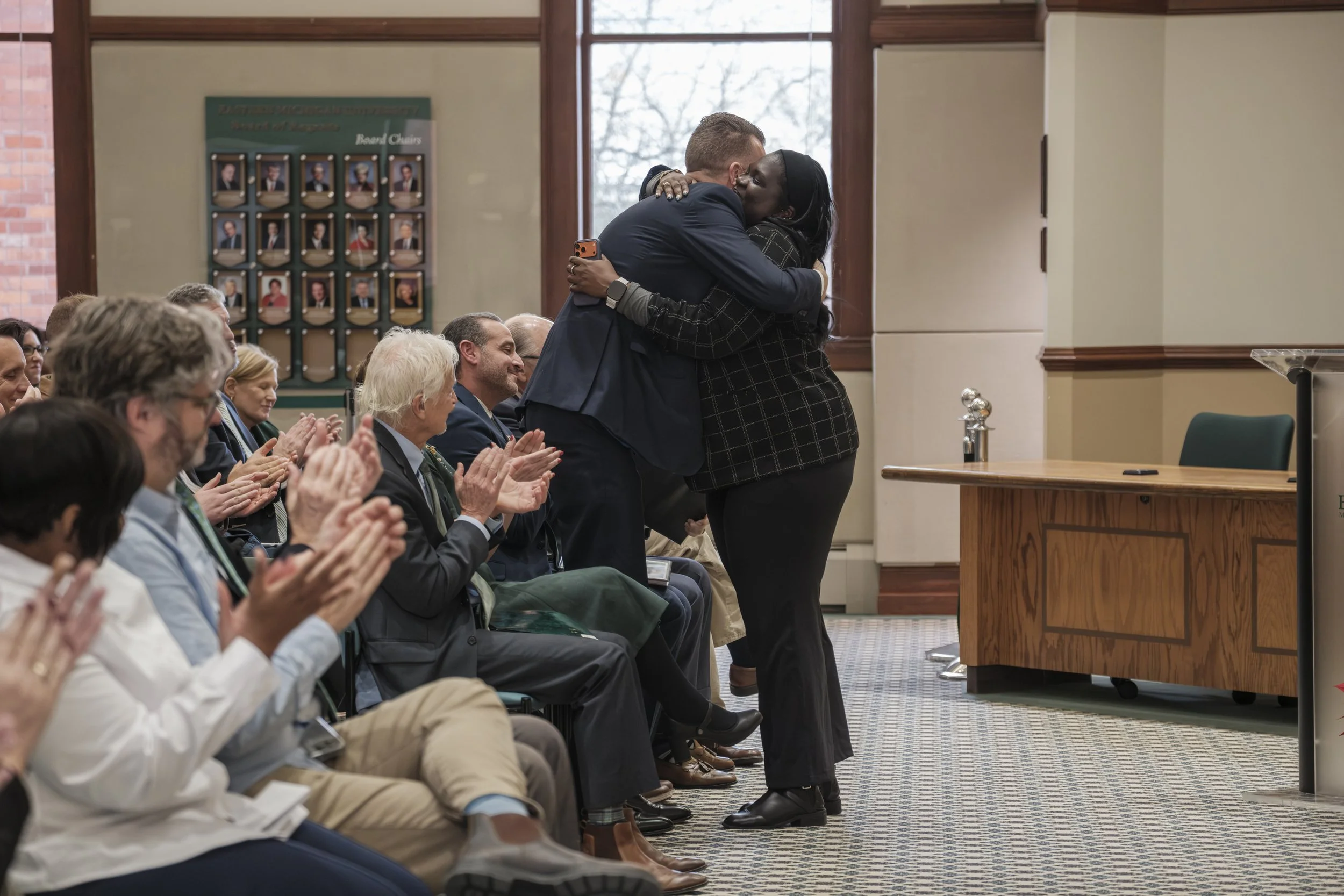 A candid photo of Ypsilanti Major Nicole Brown hugging Dr. Brendan Kelly while the audience claps in Welch Hall on the campus of Eastern Michigan University in Ypsilanti, Michigan.