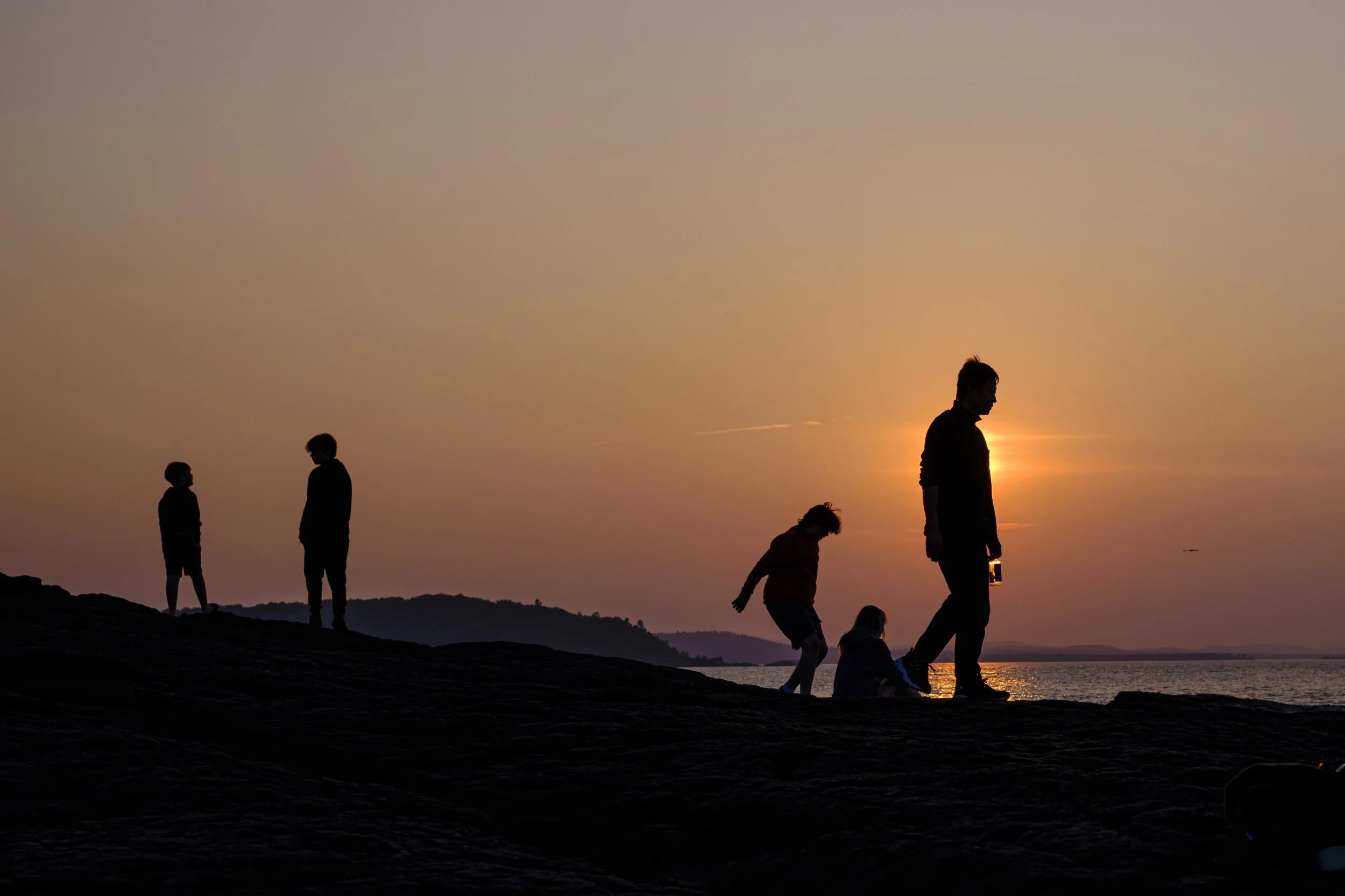A photo of people silhouetted by a sunset on Blackrocks, a popular tourist destination in Marquette, Michigan